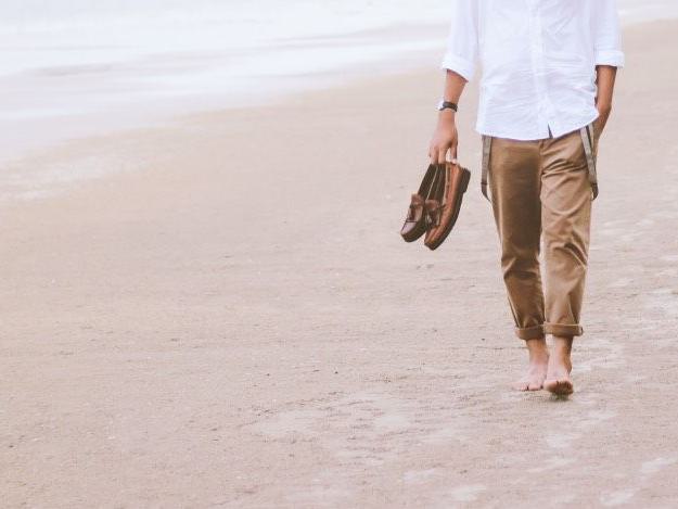 ein Mann geht barfuß am Strand mit seinen Schuhen in der Hand