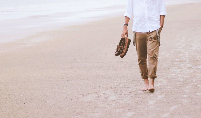 ein Mann geht barfuß am Strand mit seinen Schuhen in der Hand